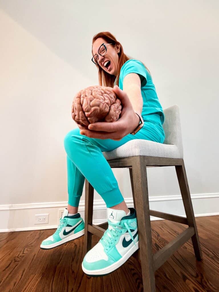 Dr. Grunch seated wearing turquoise scrubs holding model of brain